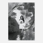 A black and white poster print featuring a woman in a white sweatshirt with a circular graphic, standing in a surreal, circular, cloud-like environment. The poster is shown hanging against a light gray wall.