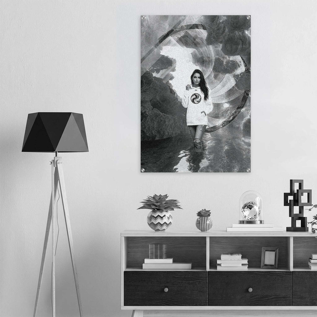 A black and white art print featuring a young girl in a white t-shirt standing in water, displayed on a light gray wall above a modern white and black sideboard with a black tripod floor lamp on the left.