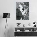 A black and white art print featuring a young girl in a white t-shirt standing in water, displayed on a light gray wall above a modern white and black sideboard with a black tripod floor lamp on the left.