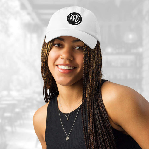 Front portrait of a smiling woman wearing the FFD16 x Under Armour Stamp Cap; the cap’s curved brim and bold black FFD monogram stand out above her long braids, with the background softly blurred.