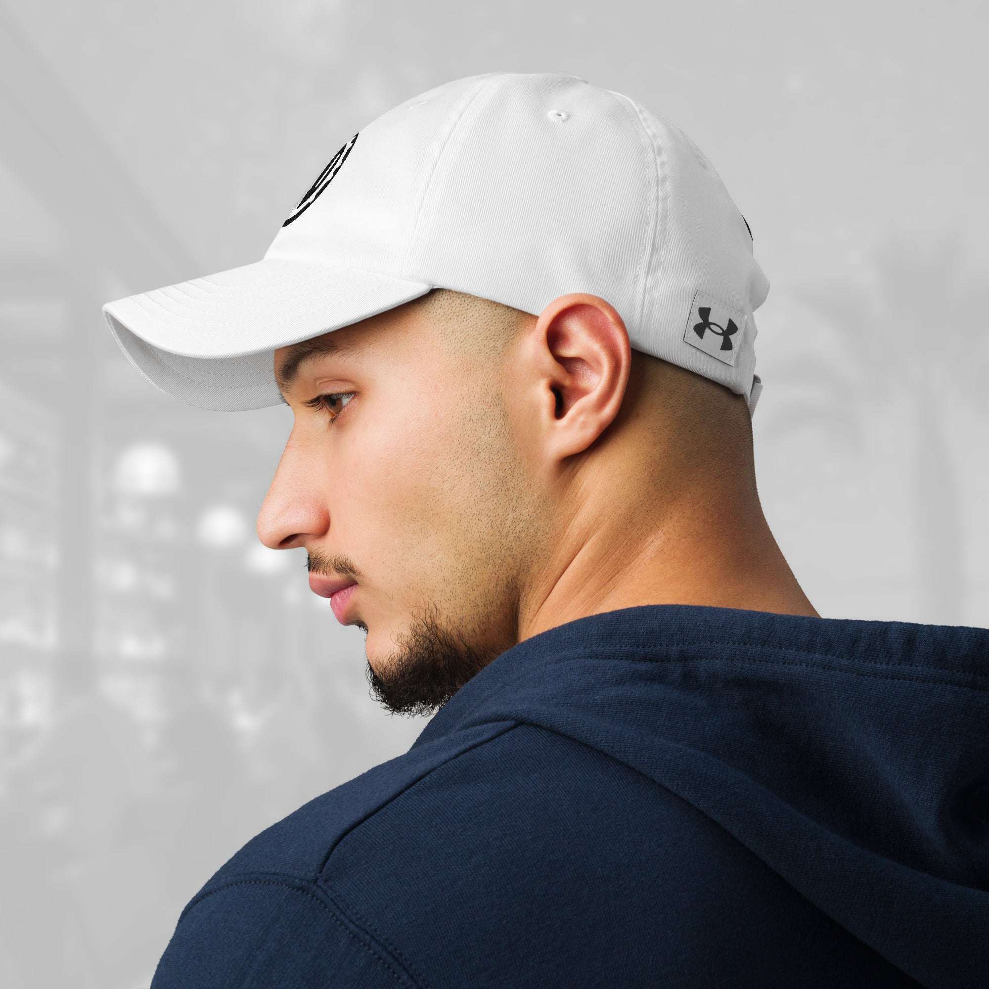 Profile of a man wearing the white FFD2 x Under Armour Stamp Cap; the black Under Armour logo on the left side of the cap is visible along with the curved brim and tonal eyelets.