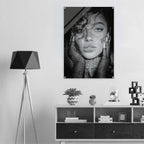 A black and white portrait poster of a woman with dramatic makeup and textured clothing, displayed on a light gray wall above a modern white and dark wood cabinet. A black tripod floor lamp stands to the left.