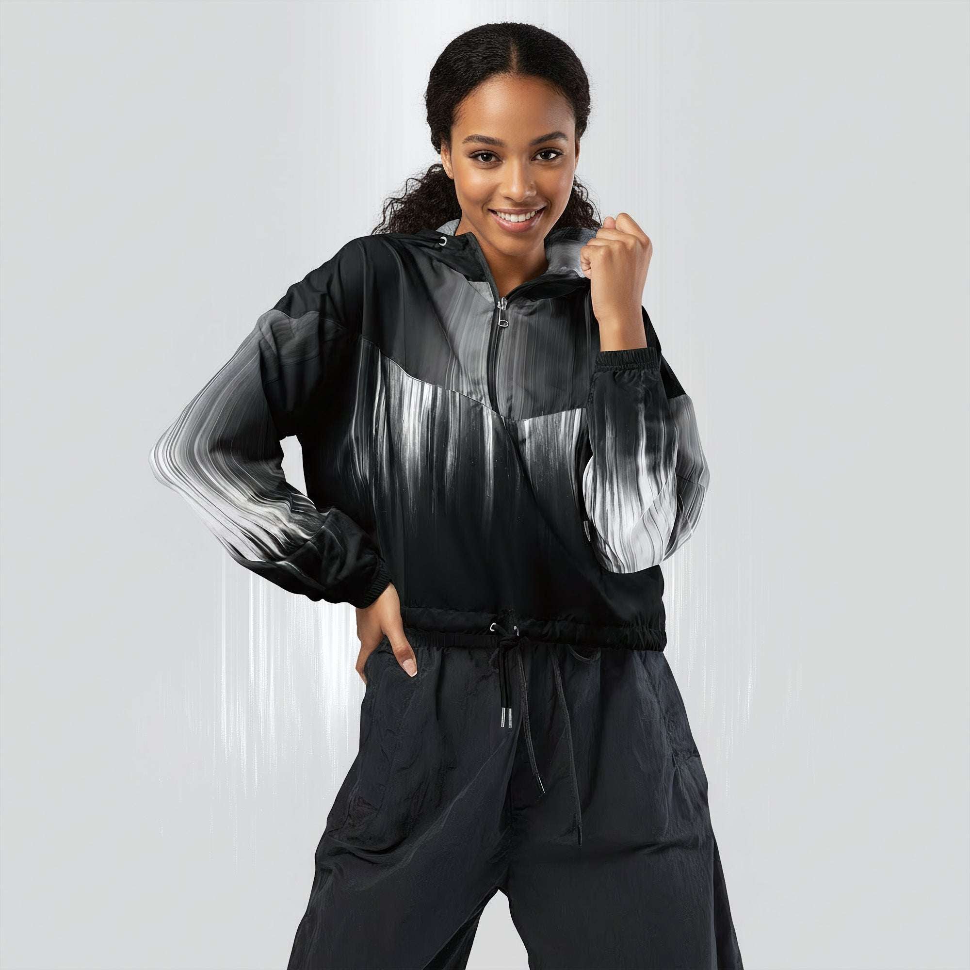 Female model wearing the HER Cropped Dither Distortion Windbreaker (No.02), three‑quarter front view. The cropped windbreaker has a black‑to‑white dither gradient pattern, long sleeves and a half‑zip front. The model holds the collar with one hand, the hood is down, and the jacket is paired with black trousers against a light grey background
