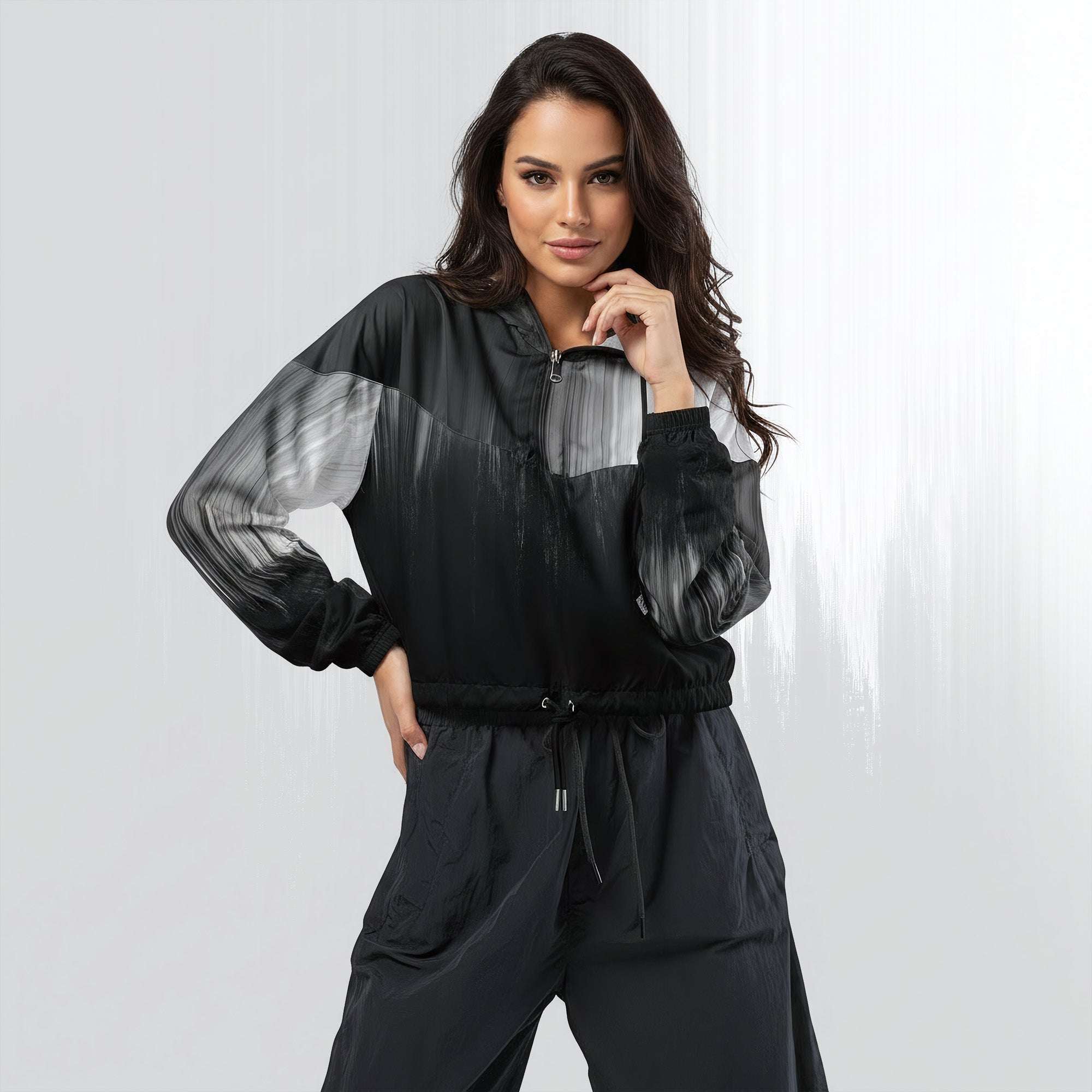 Female model wearing the HER Cropped Dither Distortion Windbreaker (No.10), three‑quarter front view. The cropped windbreaker has a black‑to‑white dither gradient pattern, long sleeves and a half‑zip front. The model holds the collar with one hand, the hood is down, and the jacket is paired with black trousers against a light grey background