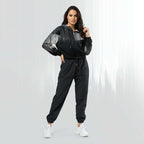 Full‑body view of a model standing in the HER Cropped Dither Distortion Windbreaker (No.10). The hooded jacket, with its abstract black‑to‑white gradient print and half‑zip closure, is worn with black trousers and white shoes. The scene has a minimalist grey background