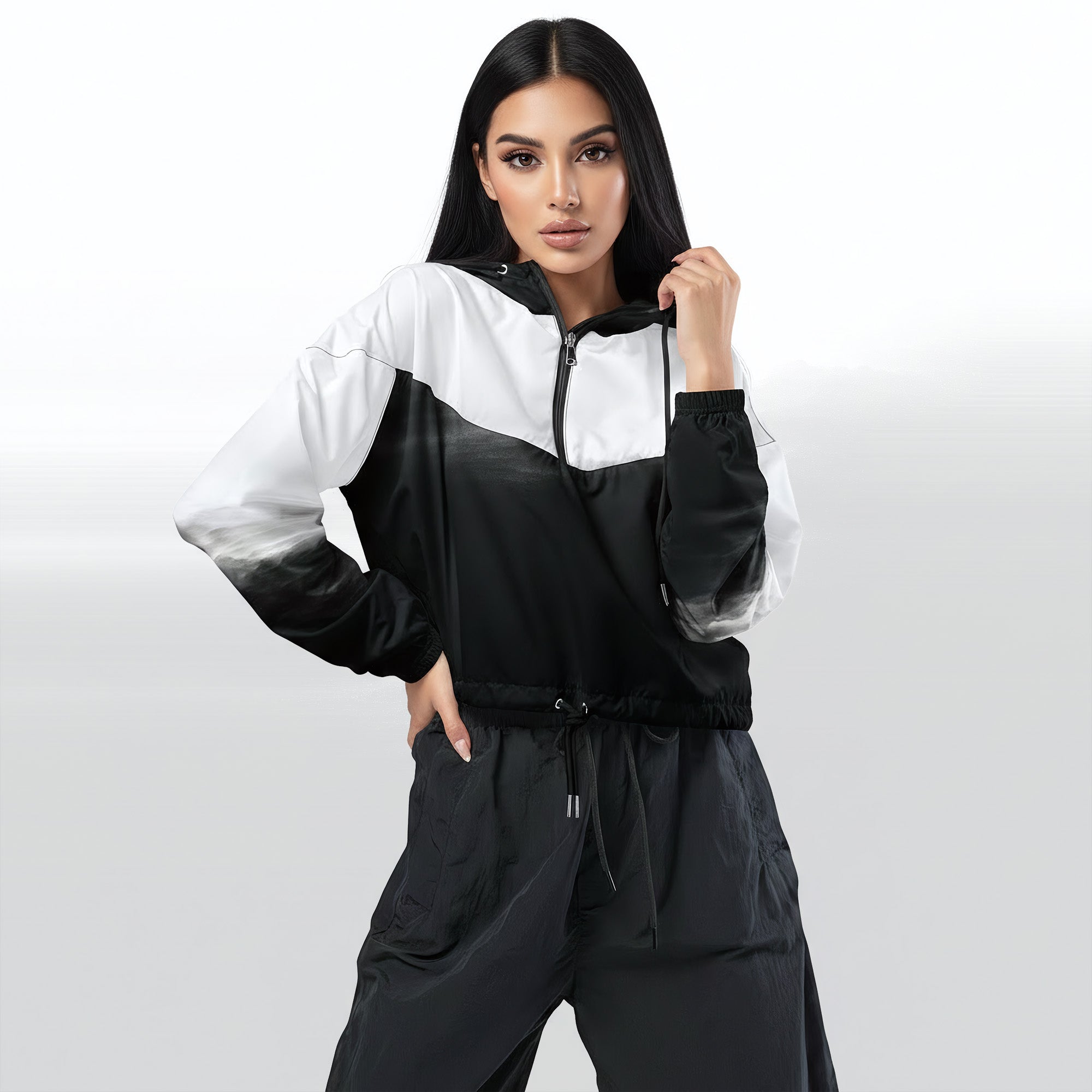 Female model wearing the HER Cropped Dither Distortion Windbreaker (No.03), three‑quarter front view. The cropped windbreaker has a black‑to‑white dither gradient pattern, long sleeves and a half‑zip front. The model holds the collar with one hand, the hood is down, and the jacket is paired with black trousers against a light grey background