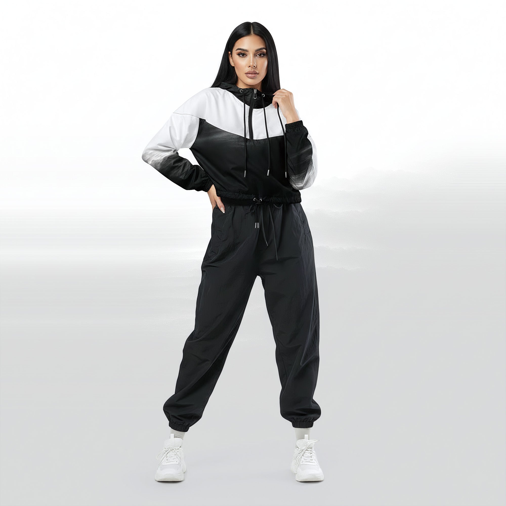 Full‑body view of a model standing in the HER Cropped Dither Distortion Windbreaker (No.03). The hooded jacket, with its abstract black‑to‑white gradient print and half‑zip closure, is worn with black trousers and white shoes. The scene has a minimalist grey background