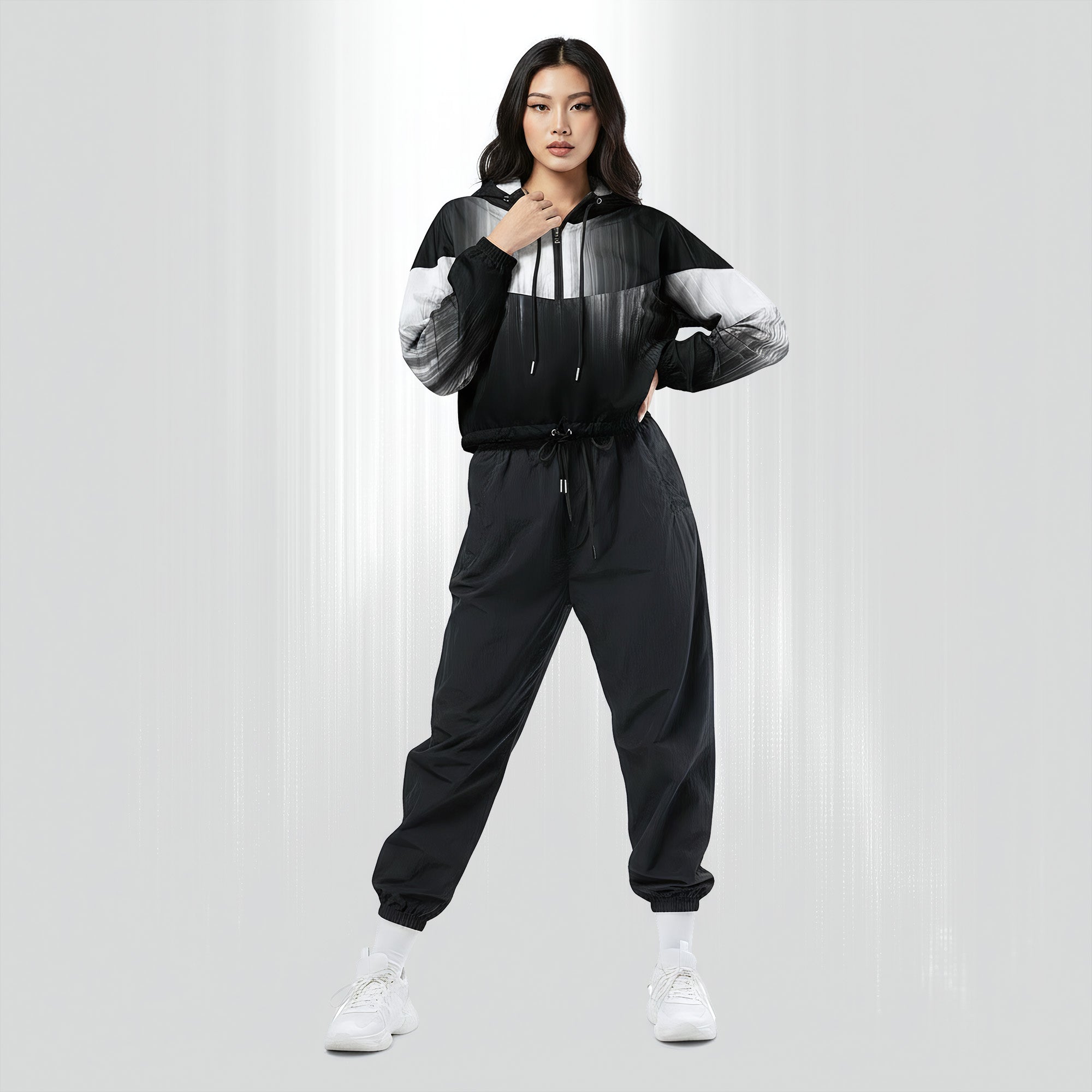 Full‑body view of a model standing in the HER Cropped Dither Distortion Windbreaker (No.04). The hooded jacket, with its abstract black‑to‑white gradient print and half‑zip closure, is worn with black trousers and white shoes. The scene has a minimalist grey background