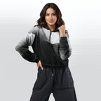 Female model wearing the HER Cropped Dither Distortion Windbreaker (No.05), three‑quarter front view. The cropped windbreaker has a black‑to‑white dither gradient pattern, long sleeves and a half‑zip front. The model holds the collar with one hand, the hood is down, and the jacket is paired with black trousers against a light grey background