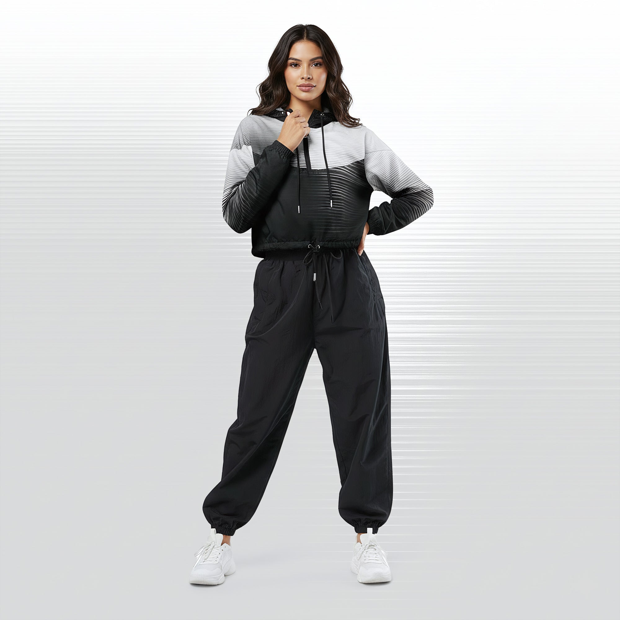 Full‑body view of a model standing in the HER Cropped Dither Distortion Windbreaker (No.05). The hooded jacket, with its abstract black‑to‑white gradient print and half‑zip closure, is worn with black trousers and white shoes. The scene has a minimalist grey background