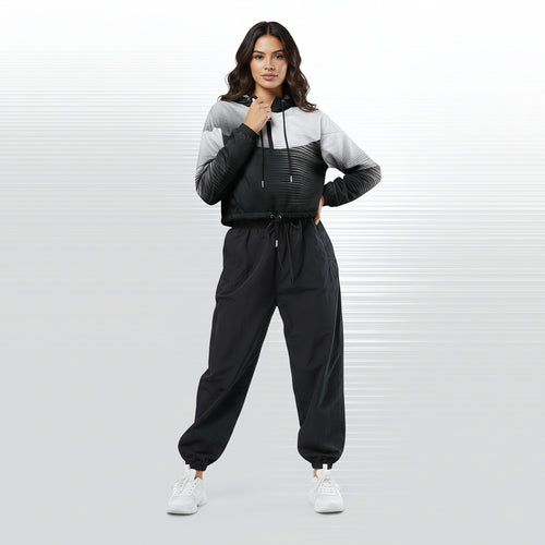 Full‑body view of a model standing in the HER Cropped Dither Distortion Windbreaker (No.05). The hooded jacket, with its abstract black‑to‑white gradient print and half‑zip closure, is worn with black trousers and white shoes. The scene has a minimalist grey background