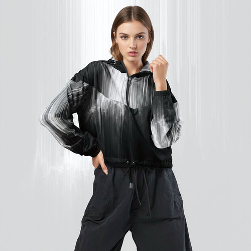 Female model wearing the HER Cropped Dither Distortion Windbreaker (No.06), three‑quarter front view. The cropped windbreaker has a black‑to‑white dither gradient pattern, long sleeves and a half‑zip front. The model holds the collar with one hand, the hood is down, and the jacket is paired with black trousers against a light grey background