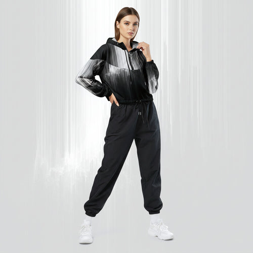 Full‑body view of a model standing in the HER Cropped Dither Distortion Windbreaker (No.06). The hooded jacket, with its abstract black‑to‑white gradient print and half‑zip closure, is worn with black trousers and white shoes. The scene has a minimalist grey background
