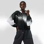 Female model wearing the HER Cropped Dither Distortion Windbreaker (No.07), three‑quarter front view. The cropped windbreaker has a black‑to‑white dither gradient pattern, long sleeves and a half‑zip front. The model holds the collar with one hand, the hood is down, and the jacket is paired with black trousers against a light grey background