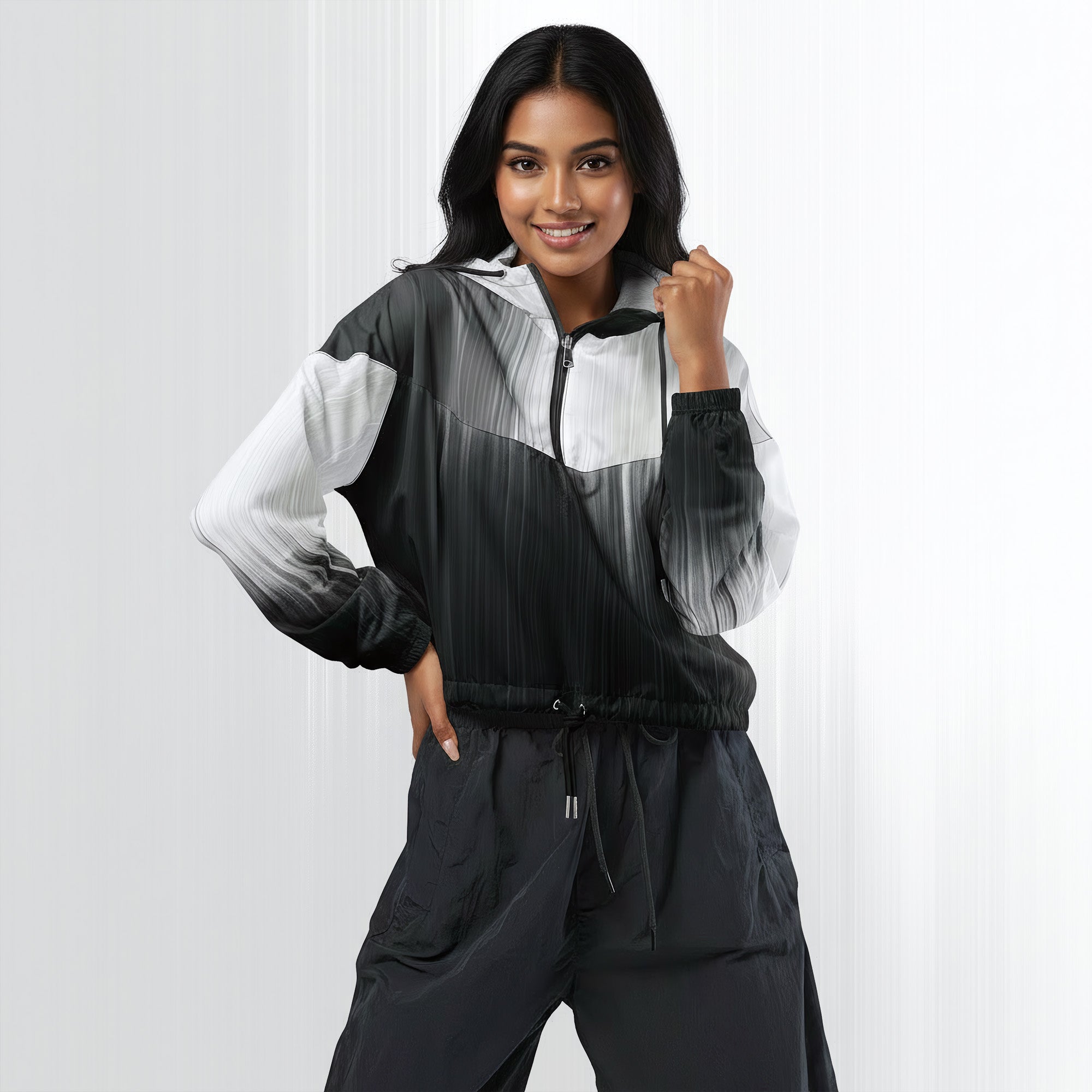 Female model wearing the HER Cropped Dither Distortion Windbreaker (No.08), three‑quarter front view. The cropped windbreaker has a black‑to‑white dither gradient pattern, long sleeves and a half‑zip front. The model holds the collar with one hand, the hood is down, and the jacket is paired with black trousers against a light grey background