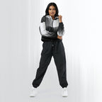 Full‑body view of a model standing in the HER Cropped Dither Distortion Windbreaker (No.08). The hooded jacket, with its abstract black‑to‑white gradient print and half‑zip closure, is worn with black trousers and white shoes. The scene has a minimalist grey background