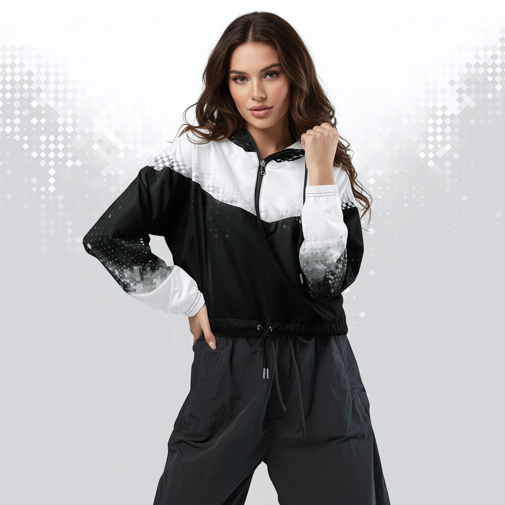 A woman modeling a black and white color-blocked zip-up windbreaker jacket with gradient sleeve details, paired with dark gray drawstring pants, against a light gray background with subtle digital diamond patterns.