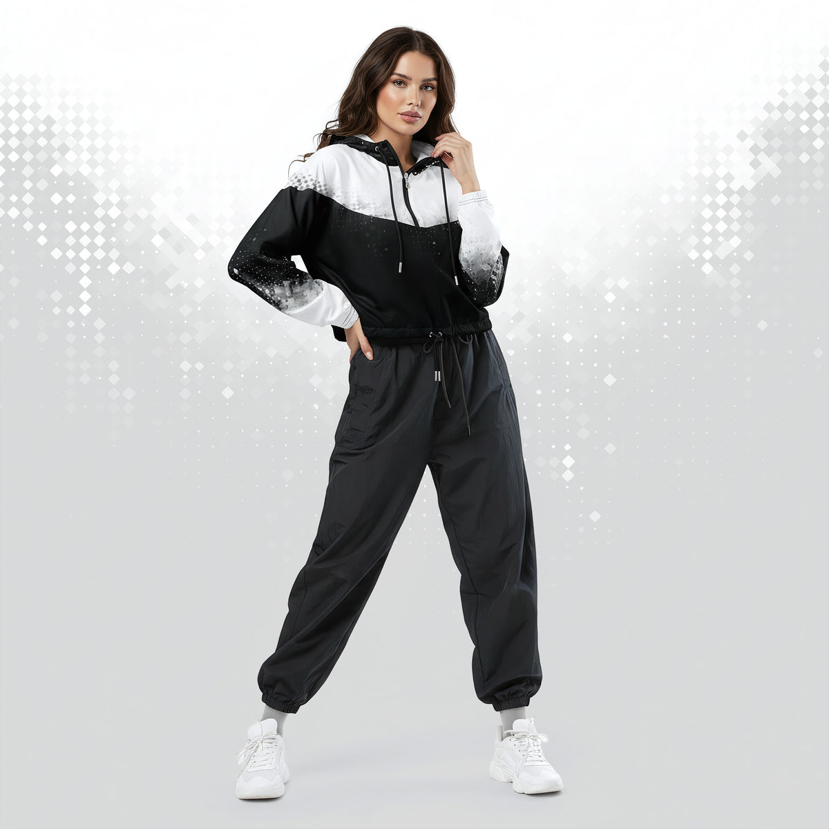 A woman modeling a black and white color-blocked windbreaker jacket with matching black jogger pants and white sneakers, posed against a light gray studio background with a subtle dotted pattern.