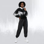 A model wearing a black and white abstract-patterned zip-up hoodie with black jogger pants and white sneakers, standing against a light gray background with vertical white streaks.