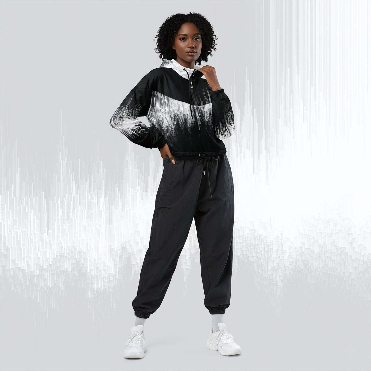 A model wearing a black and white abstract-patterned zip-up hoodie with black jogger pants and white sneakers, standing against a light gray background with vertical white streaks.
