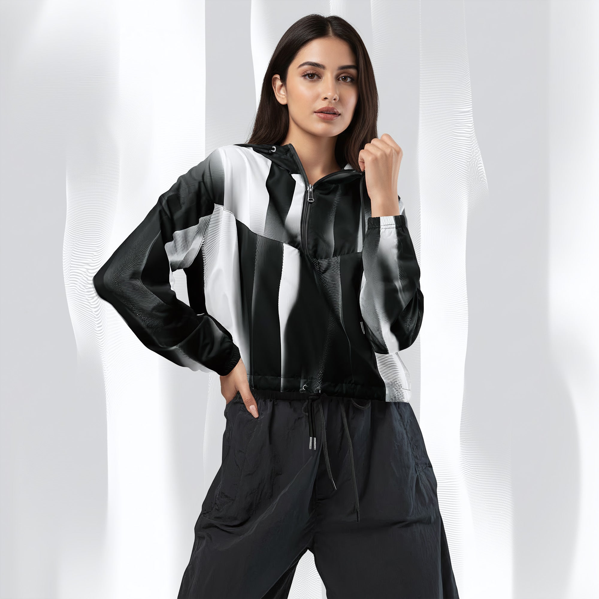 A woman modeling a black and white striped zip-up jacket with matching dark pants, posed against a white draped studio backdrop.