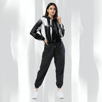 A woman modeling a black, white, and gray color-blocked zip-up hoodie with matching black jogger pants and white sneakers, set against a white background with soft vertical shadows.