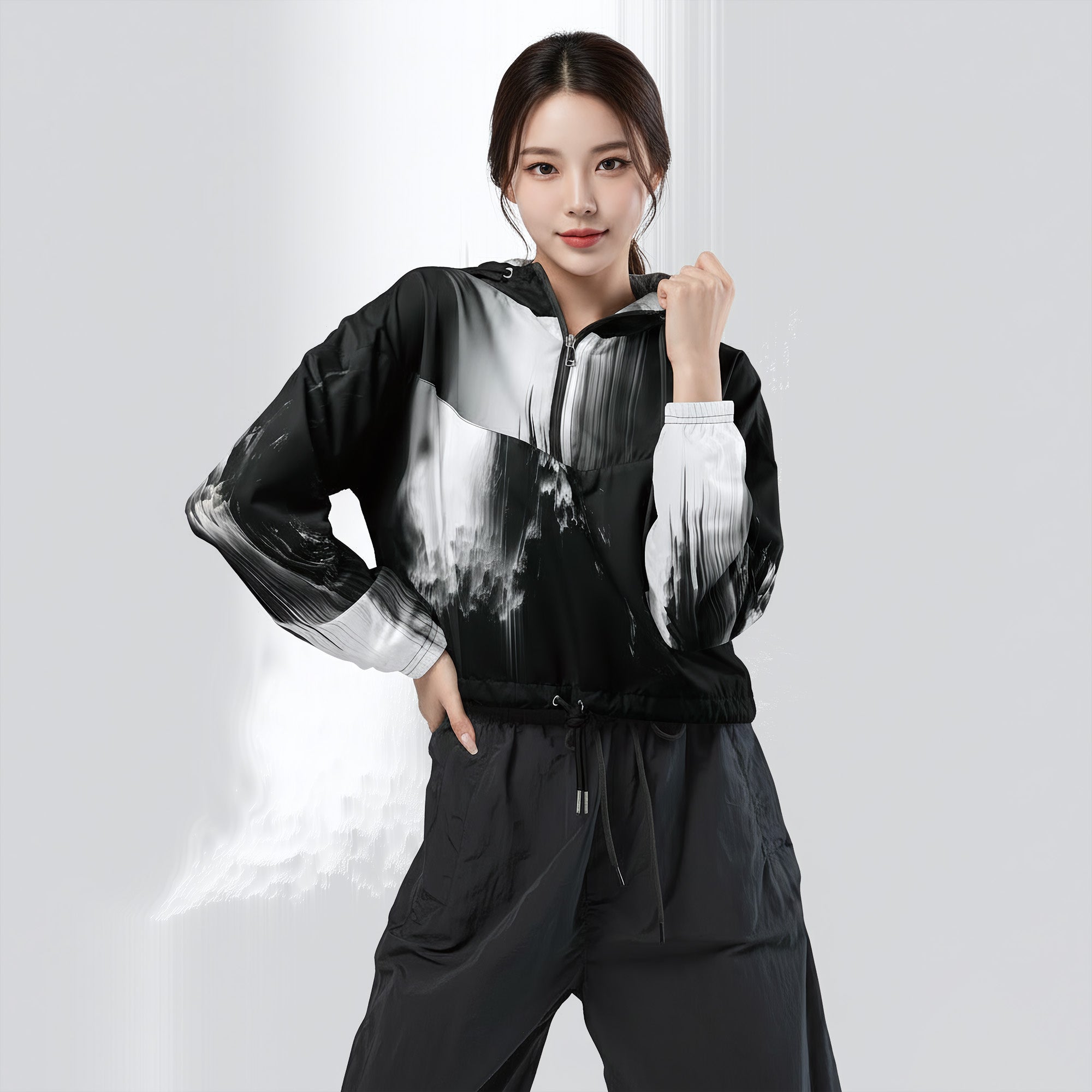 A woman modeling a black and white abstract print zip-up windbreaker jacket with matching black drawstring pants against a light gray studio background.