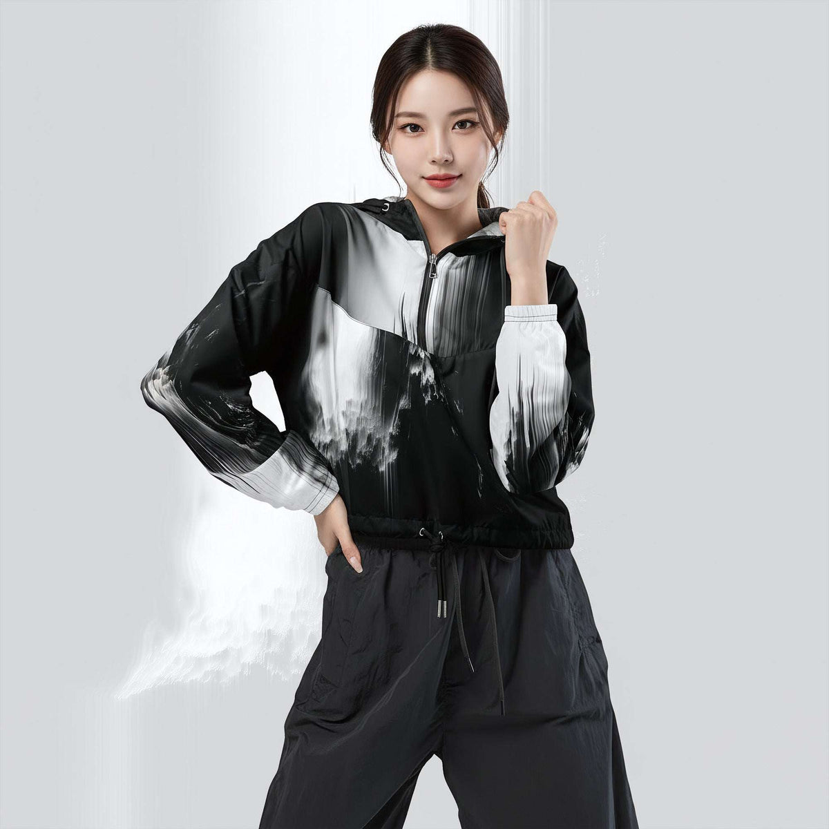 A woman modeling a black and white abstract print zip-up windbreaker jacket with matching black drawstring pants against a light gray studio background.
