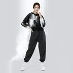 A woman modeling a black and white graphic hoodie with matching black jogger sweatpants and white sneakers, standing against a light gray studio background with a stylized white smoke effect.