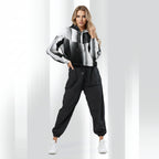 A woman modeling a black, white, and gray color-blocked cropped hoodie with black jogger pants and white sneakers, standing against a white studio background with vertical light stripes.