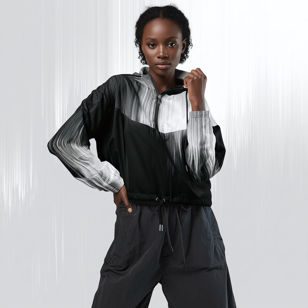 A model wearing a black, white, and gray color-blocked zip-up jacket with matching dark gray pants, posing against a light gray studio background with vertical light streaks.