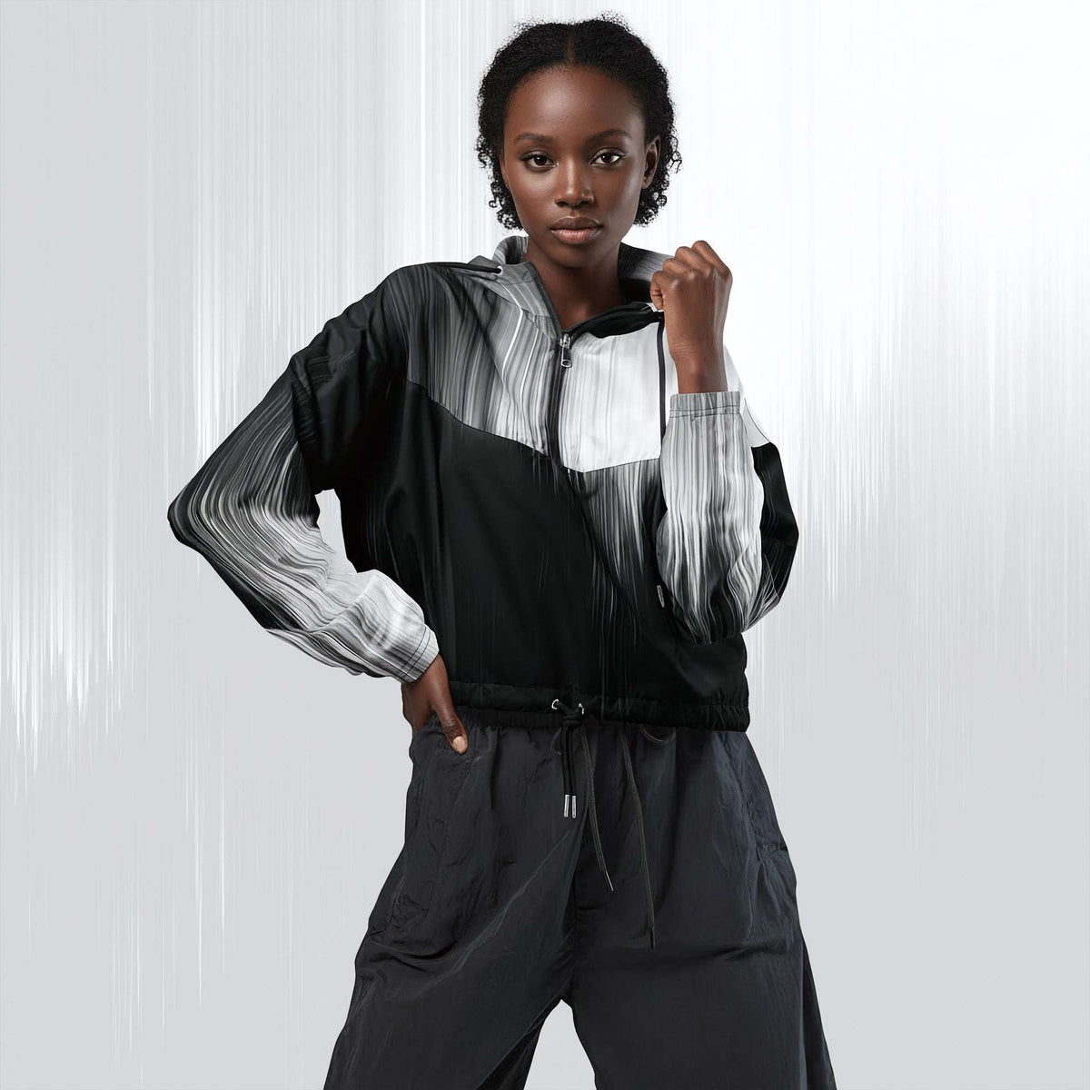 A model wearing a black, white, and gray color-blocked zip-up jacket with matching dark gray pants, posing against a light gray studio background with vertical light streaks.