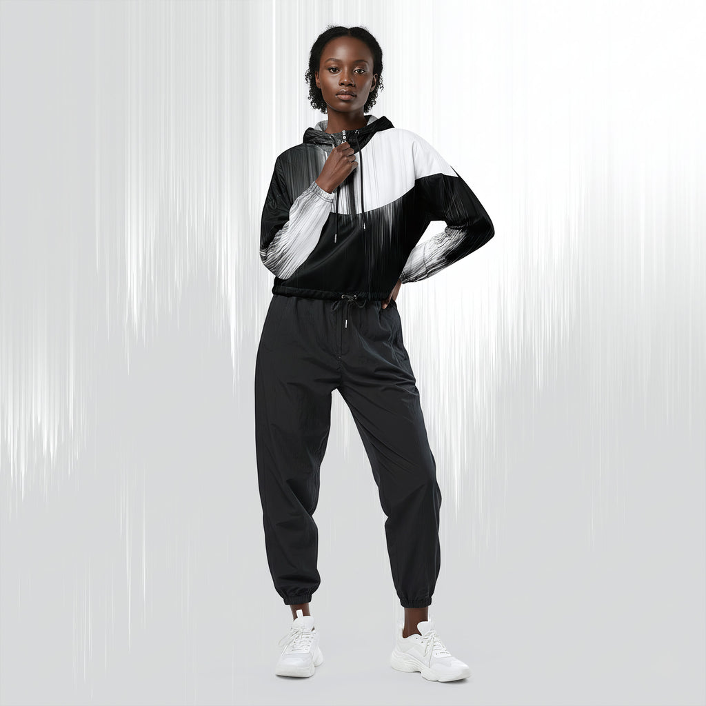 A model wearing a black and white color-blocked zip-up hoodie with matching black jogger pants and white sneakers, standing against a light gray studio background with vertical light streaks.