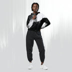 A model wearing a black and white color-blocked zip-up hoodie with matching black jogger pants and white sneakers, standing against a light gray studio background with vertical light streaks.