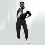 A model wearing a black and white color-blocked zip-up hoodie with matching black jogger pants and white sneakers, standing against a light gray studio background with vertical light streaks.