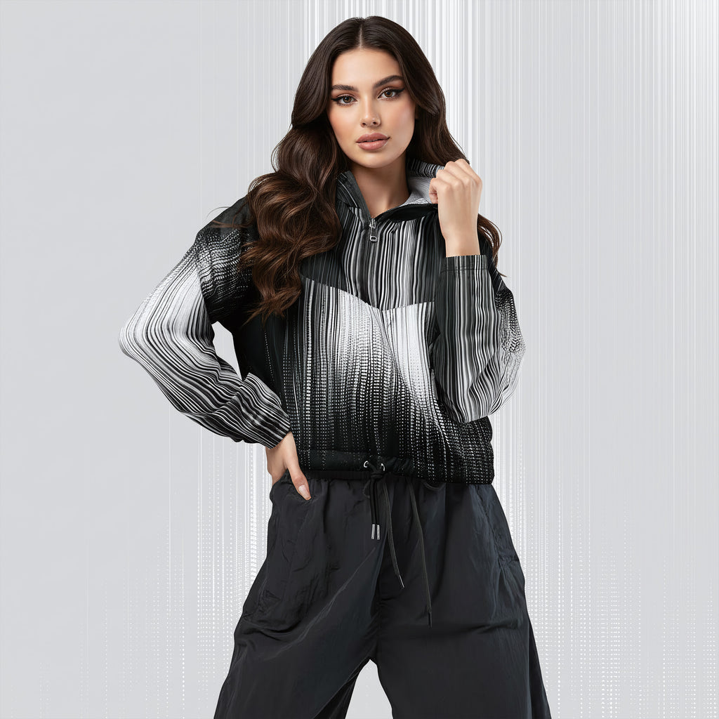 A woman modeling a black and white striped zip-up jacket with a gradient effect, paired with black pants, against a light gray textured studio background.