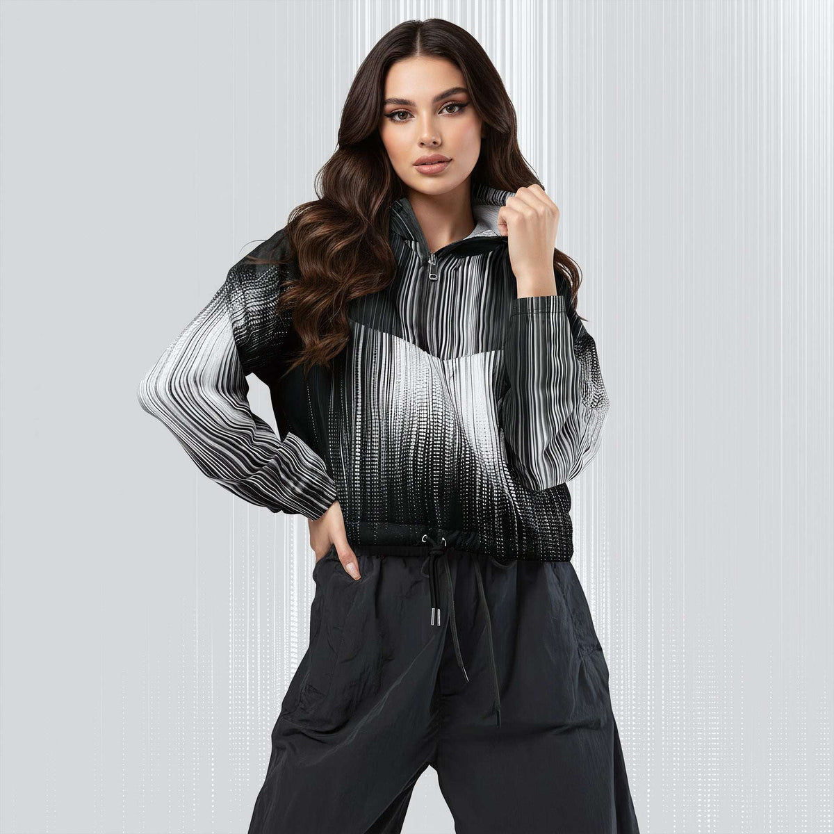 A woman modeling a black and white striped zip-up jacket with a gradient effect, paired with black pants, against a light gray textured studio background.