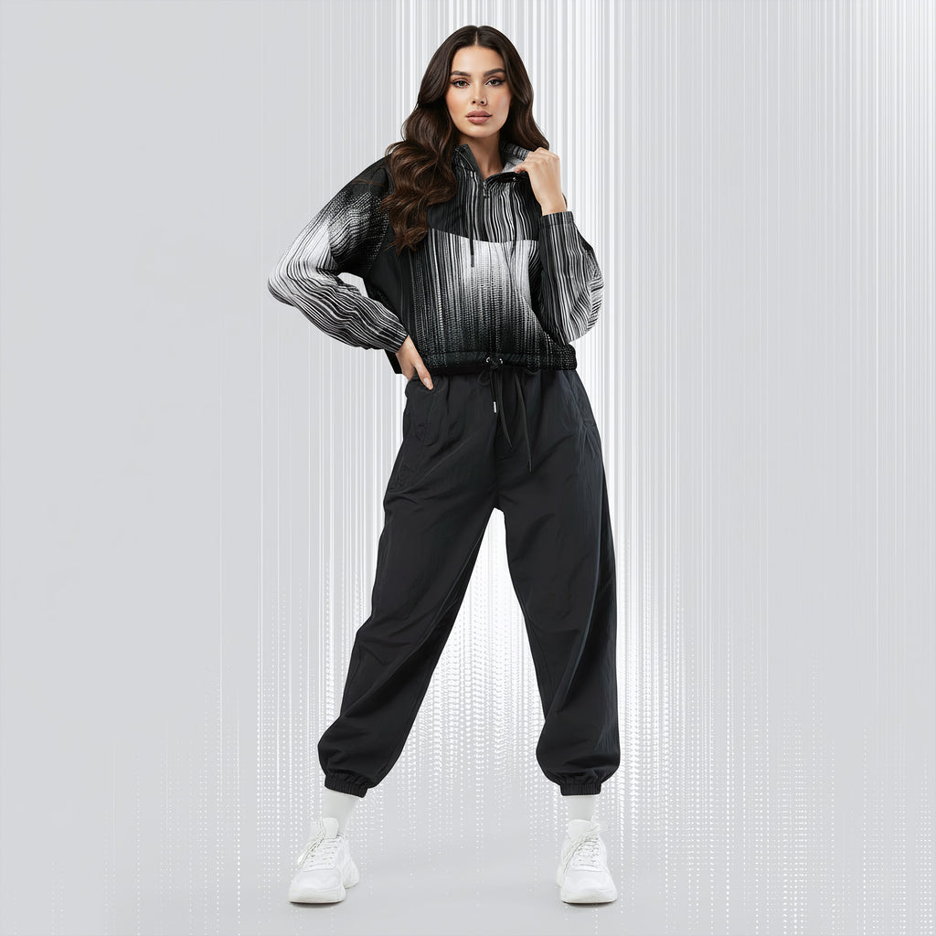 A woman modeling a black and white striped zip-up hoodie with black jogger sweatpants and white sneakers, standing against a light gray textured studio background.