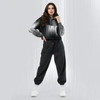 A woman modeling a black and white striped zip-up hoodie with black jogger sweatpants and white sneakers, standing against a light gray textured studio background.
