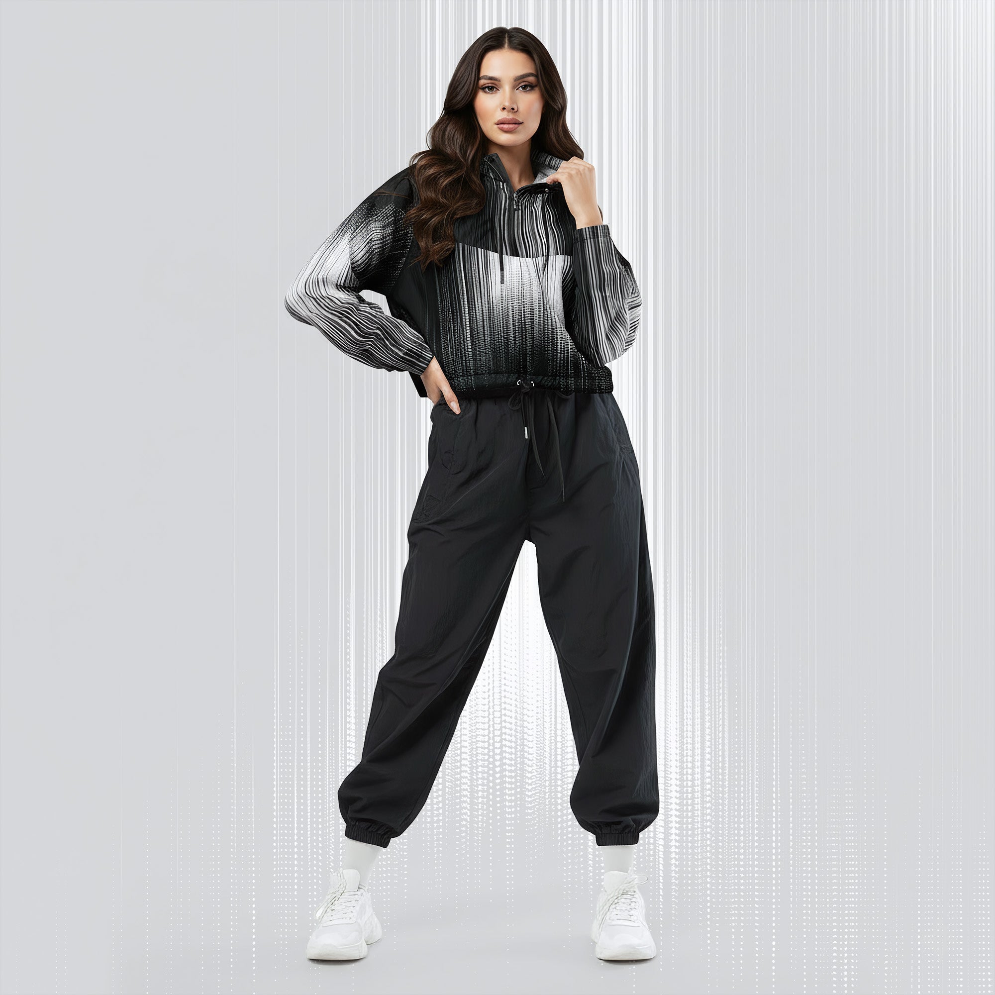 A woman modeling a black and white striped zip-up hoodie with black jogger sweatpants and white sneakers, standing against a light gray textured studio background.
