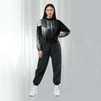 A woman modeling a black and gray gradient patterned hooded windbreaker jacket with matching black jogger pants and white sneakers, set against a light gray studio background with vertical light streaks.