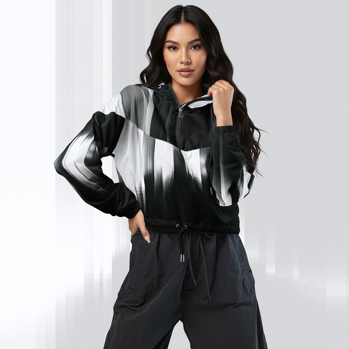 A woman modeling a black, white, and gray color-blocked zip-up jacket with a matching black drawstring pants set, posed against a light gray studio background.