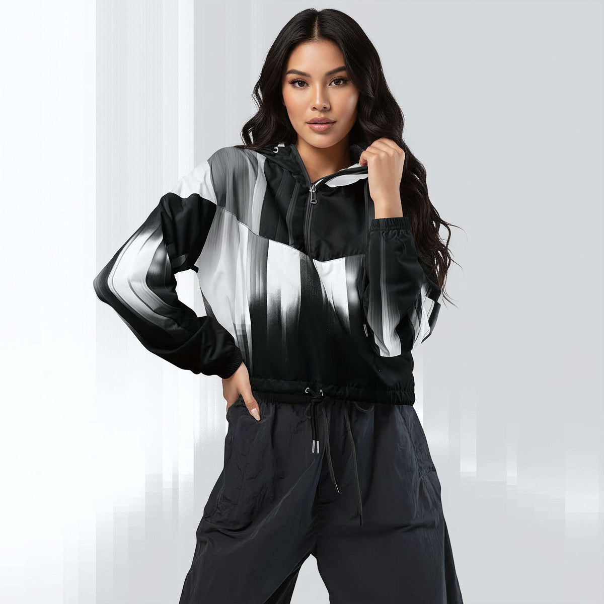 A woman modeling a black, white, and gray color-blocked zip-up jacket with a matching black drawstring pants set, posed against a light gray studio background.