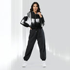 A woman modeling a black and white abstract-patterned hoodie with black jogger pants and white sneakers, standing against a light gray studio background.