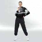 Full‑body view of a model standing in the HER Cropped Dither Distortion Windbreaker. The hooded jacket, with its abstract black‑to‑white gradient print and half‑zip closure, is worn with black trousers and white shoes. The scene has a minimalist grey background