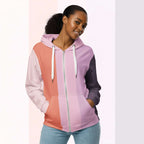 Front view of another woman wearing the Her Palette Strip Hoodie No. 14; pastel stripes cover the torso and sleeves, lavender hood lining and white zip, hands resting in the kangaroo pocket, pastel striped background from Form Finding Design.
