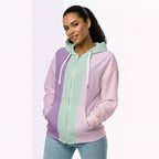 Front view of another woman wearing the Her Palette Strip Hoodie No. 19; pastel stripes cover the torso and sleeves, lavender hood lining and white zip, hands resting in the kangaroo pocket, pastel striped background from Form Finding Design.