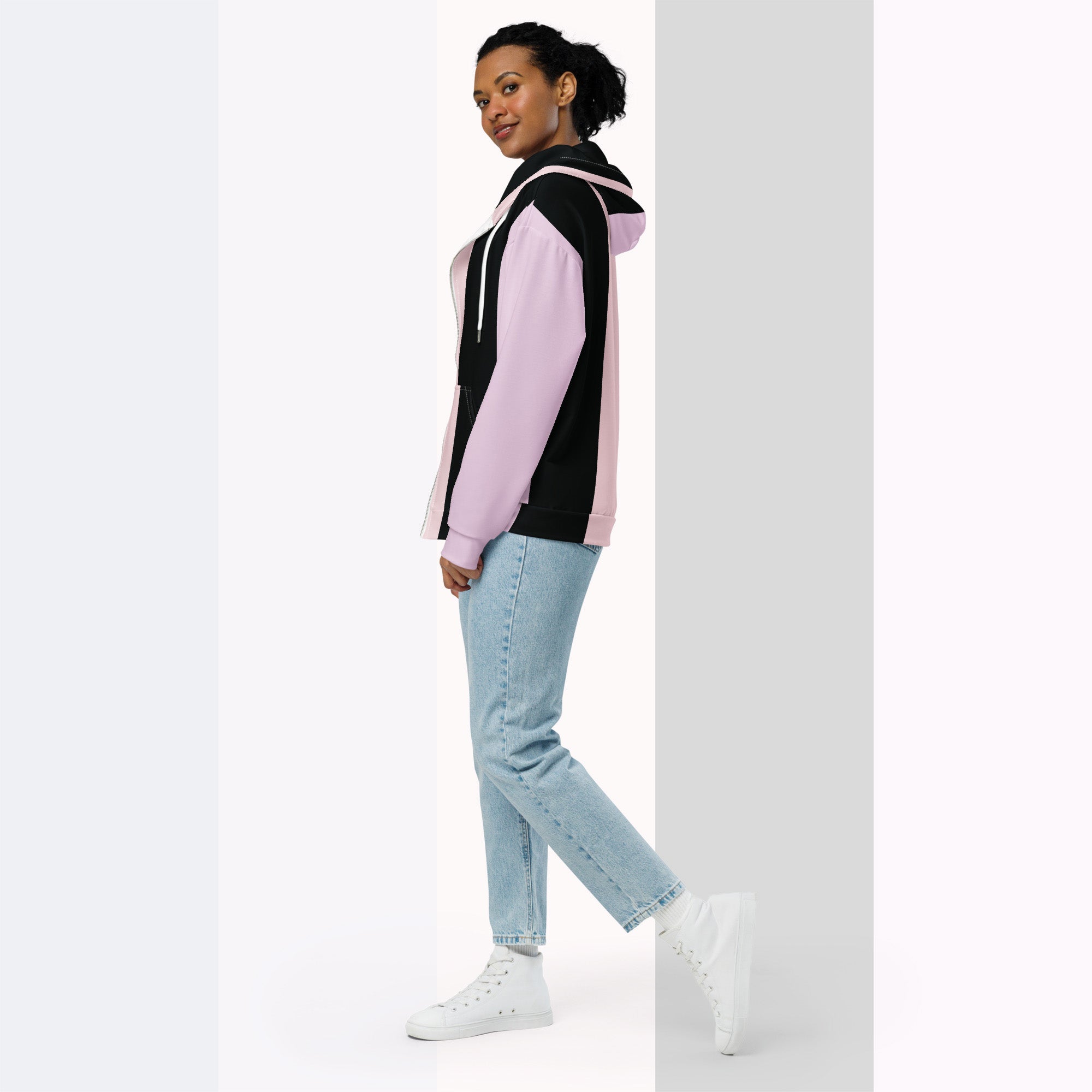 Full‑body side profile of a woman in the Her Palette Strip Hoodie No. 11; pastel vertical stripes with lavender hood and white drawstrings, styled with light blue jeans and white trainers, standing before a softly striped backdrop from Form Finding Design.