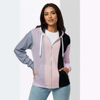 Front view of another woman wearing the Her Palette Strip Hoodie No. 11; pastel stripes cover the torso and sleeves, lavender hood lining and white zip, hands resting in the kangaroo pocket, pastel striped background from Form Finding Design.