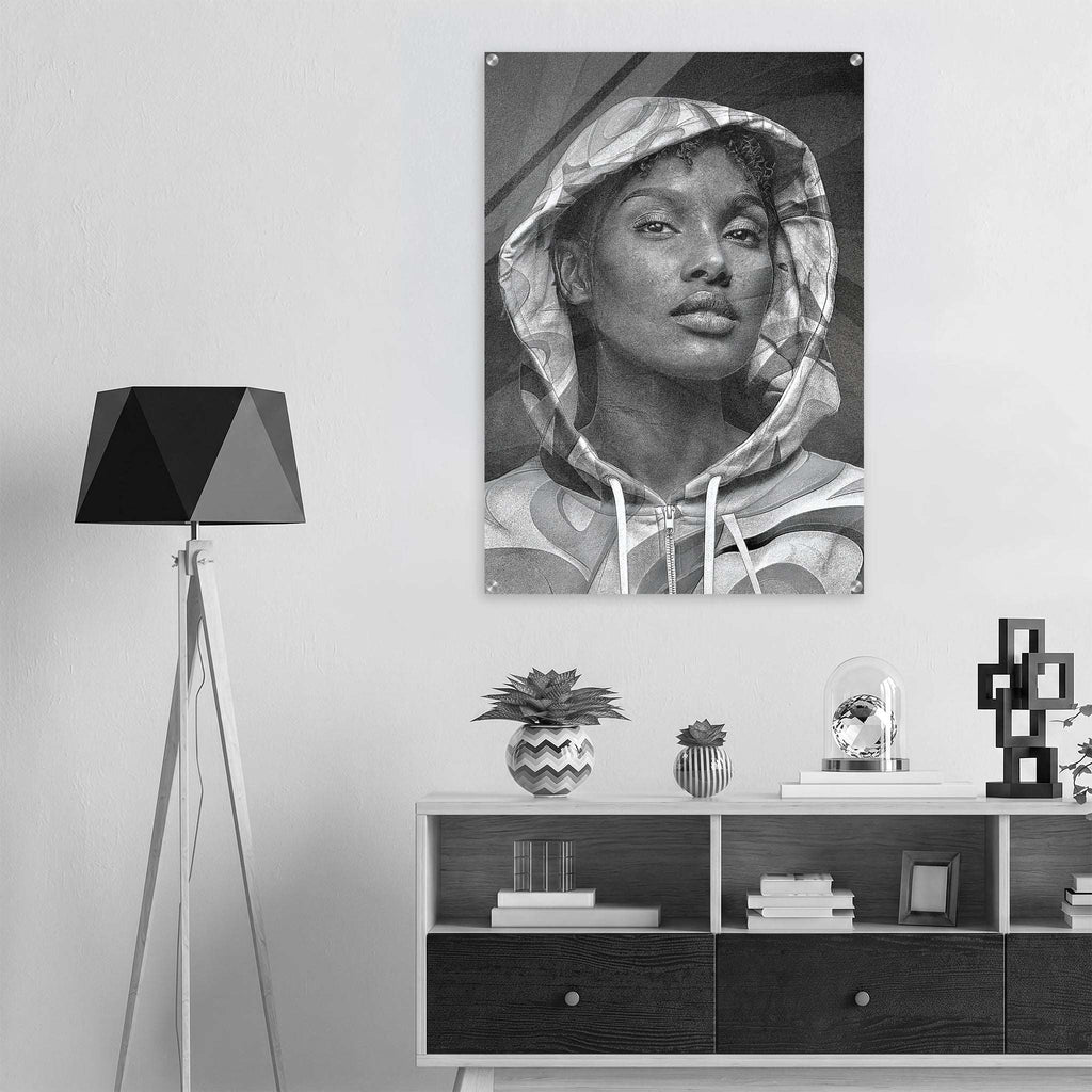 A black and white wall art print depicting a woman in a hoodie, displayed in a modern room setting above a wooden shelf with decorative items.